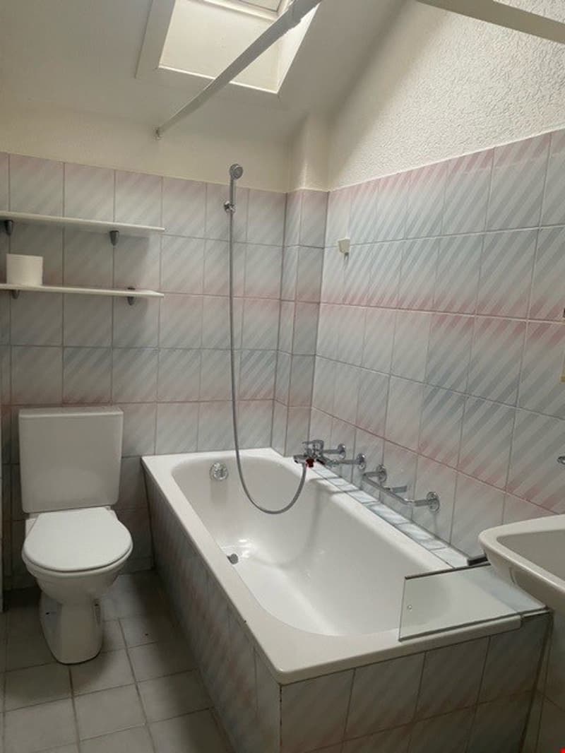 Bathroom with white toilet, bathtub, sink, and tiled walls