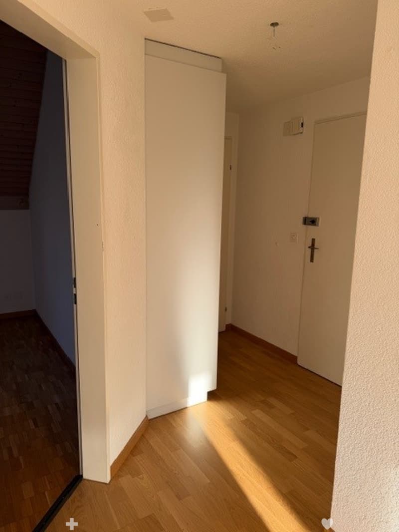 Empty room with wooden floor, white walls, two doors, one of which is open, and a small window.