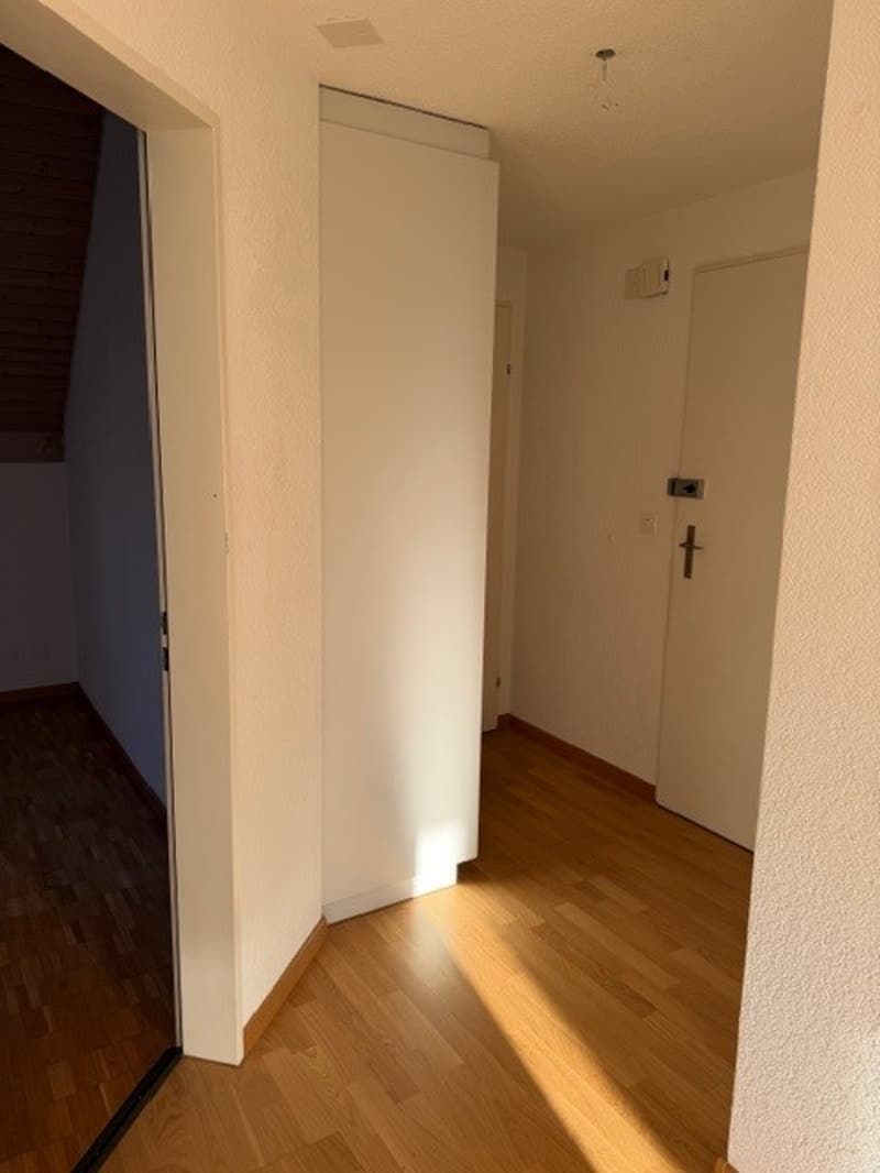 Empty room with wooden floor, white walls, two doors, one of which is open, and a small window.