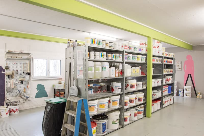 storage shelves with buckets, ladder, trash bin, equipment hanging on wall, windows with view of outdoors
