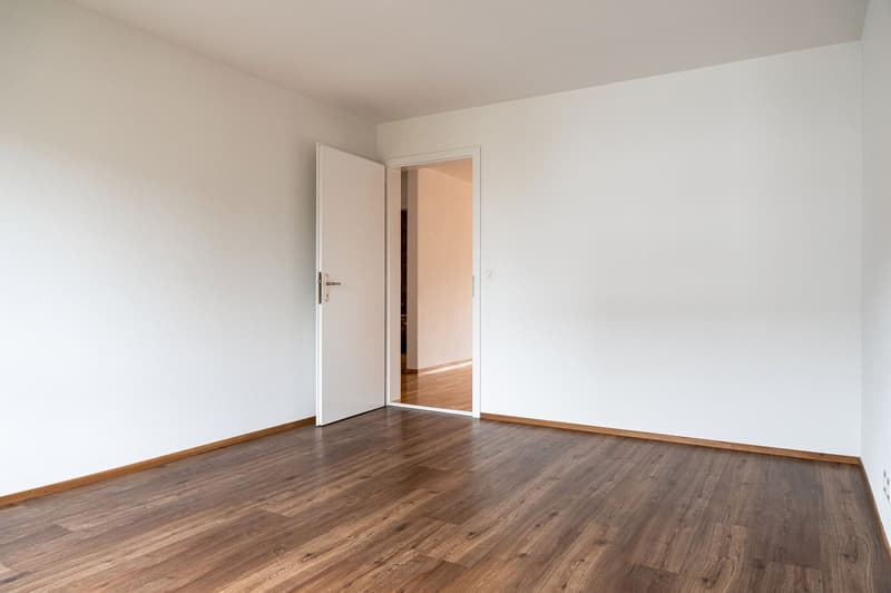 empty room, white walls, wooden floor, open door leading to another room