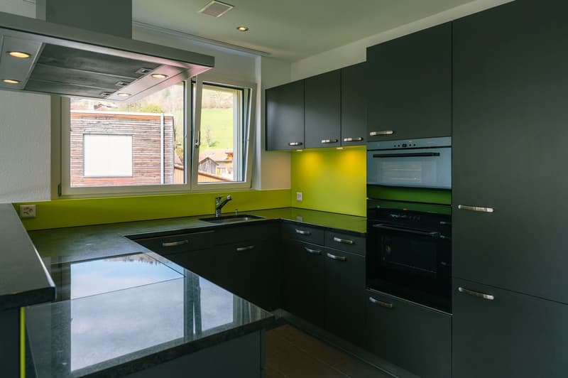modern kitchen with black cabinets, green backsplash, granite countertops, stainless steel sink, faucet, built-in oven, window with view