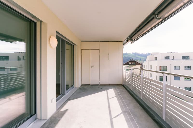 Balcony with sliding glass doors, white railings, white walls, white ceiling, white door, white cabinets, white light fixture