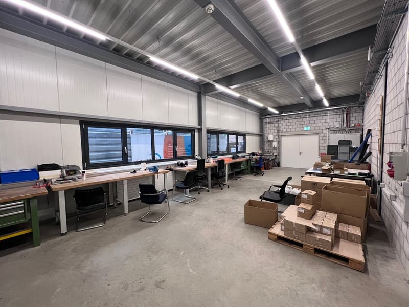 long work tables, office chairs, lots of cardboard boxes, fluorescent lighting on ceiling, large windows