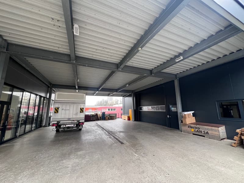 warehouse interior, metal roof, gray walls, concrete floor, boxes, truck, black doors