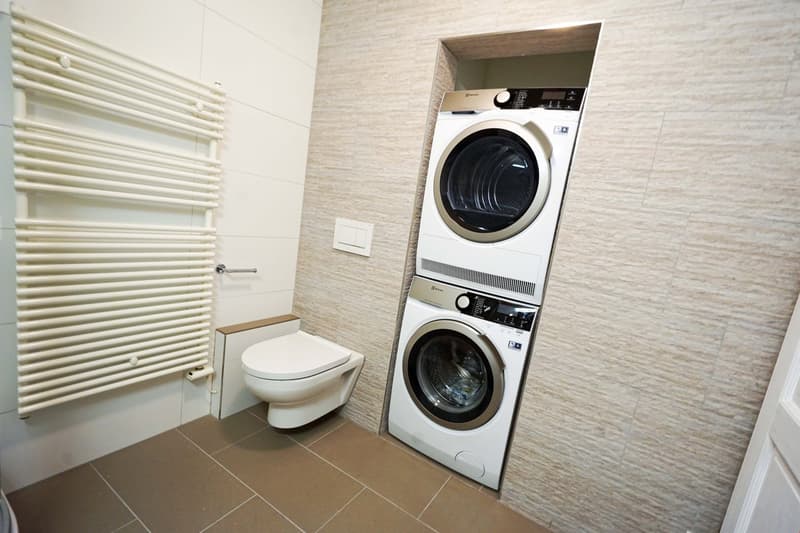 Bathroom with a stacked washer and dryer unit, toilet, and tiled walls