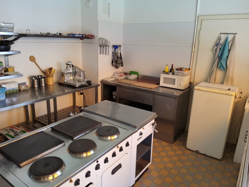 equipped with stainless steel countertops, industrial cooking appliances, shelves with various kitchen tools, a microwave oven, and a refrigerator