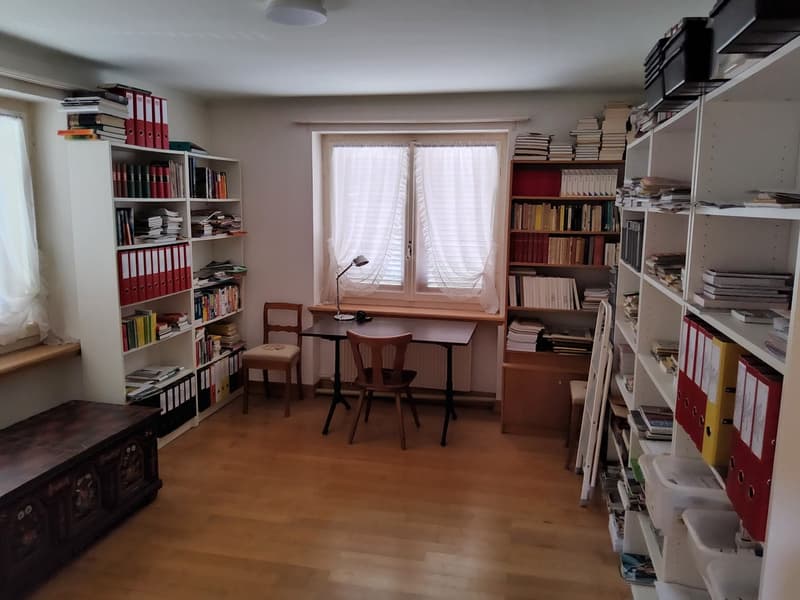 room with wooden floor, desk, chair, bookshelves, radiator, lamp, window with curtains, storage boxes, ladder