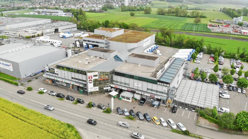 Large commercial building with multiple floors, parking lot, and surrounded by green fields and countryside