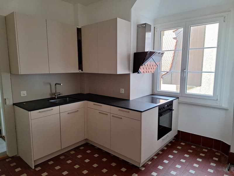 modern kitchen with white cabinets, black countertops, stainless steel sink, gas stove, oven, and a window