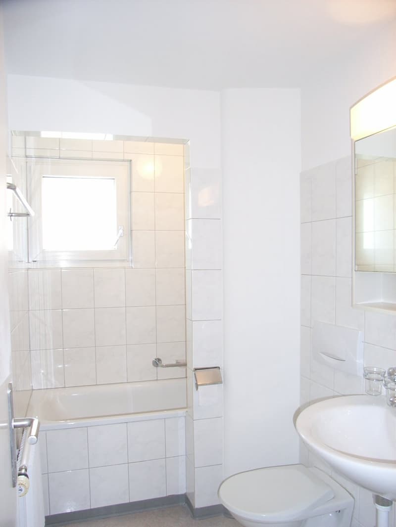 Bathroom with white tiles, bathtub, toilet, sink, mirror, and window