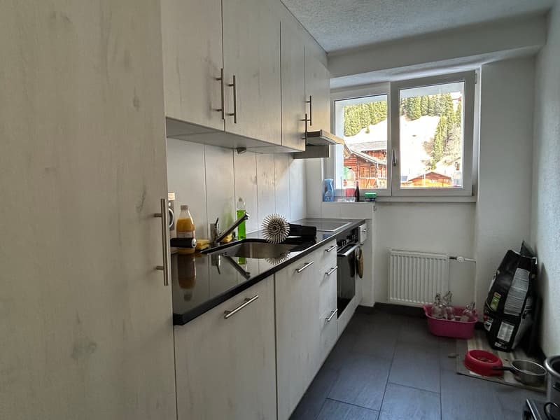 modern kitchen with white cabinets, black countertops, stainless steel sink, dishwasher, washing machine, and a window with a view