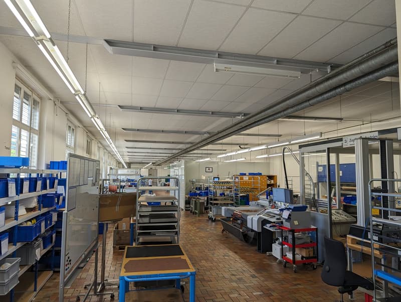 spacious warehouse, lined with shelves and equipment, brick flooring, multiple fluorescent lights on the ceiling