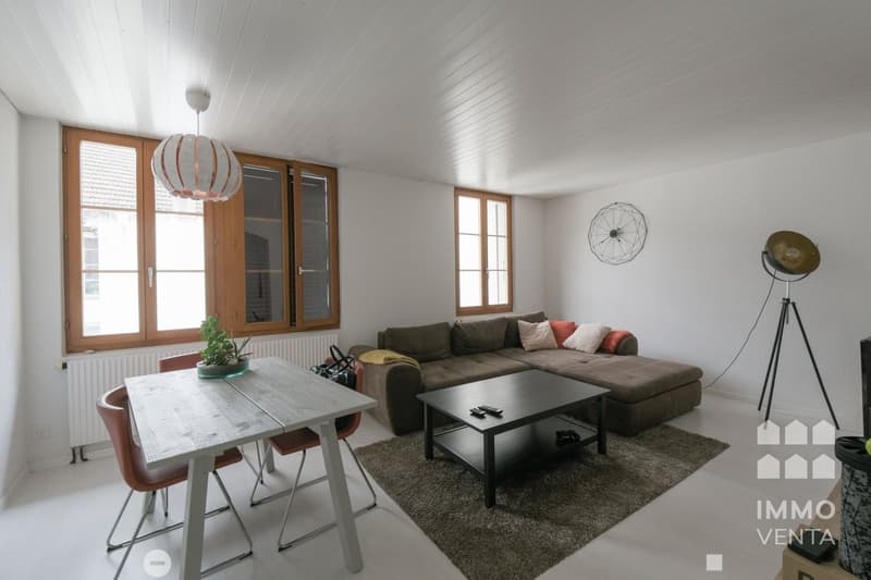 white walls, wooden windows, living room with couch, table, chairs, coffee table, radiator