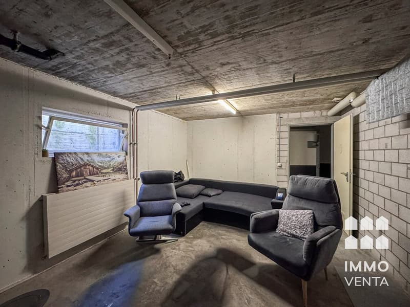 A room with a concrete ceiling, a couch, two armchairs, a window, and a radiator.