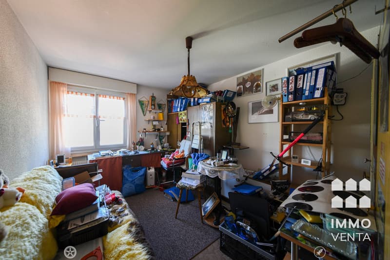cluttered room with a desk, chair, shelves, and various items