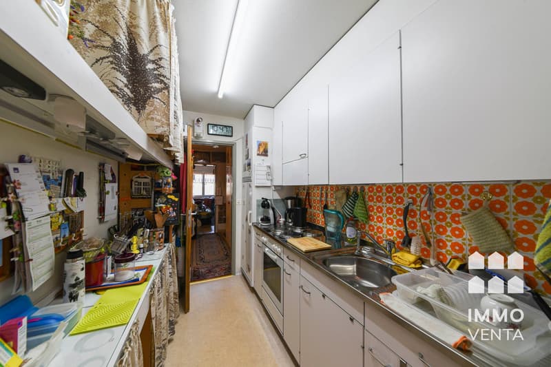 modern kitchen, white cabinets, tiled backsplash, stainless steel sink, gas stove, refrigerator, countertop, various kitchen utensils, open door to another room