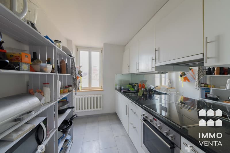 modern kitchen with white cabinets, black countertops, stainless steel appliances, white tiled floor, large window