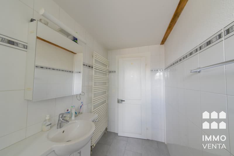 Bathroom with white tiles, white sink, mirror, towel rack, and a white door.