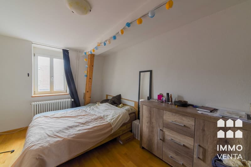 bedroom with bed, wooden floor, white walls, window, radiator, wooden cabinet, mirror, string of lights