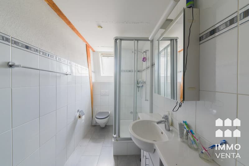 Bathroom with white tiles, glass shower, white sink, mirror, toilet, and a towel rack.