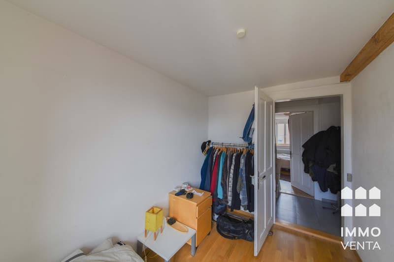 empty room, white walls, wooden floor, open closet, clothes hanging, small table, lamp, bag on floor