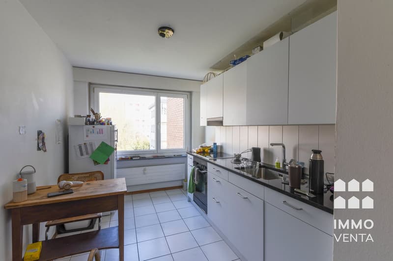 modern kitchen with white cabinets, black countertops, white tiles, large window, refrigerator, sink, oven, microwave, kettle, toaster, coffee machine, dining table, chairs, radiator