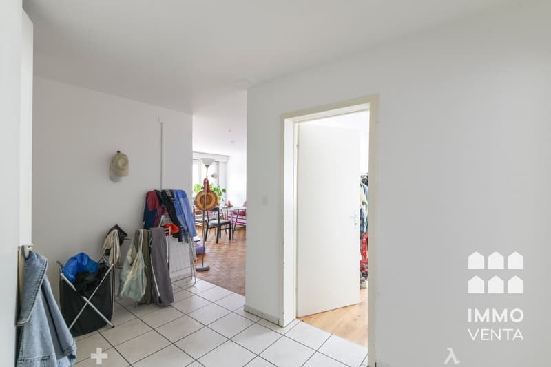 white walls, white tile floor, open door, clothes hanging, hat on wall, laundry basket, table and chairs in background