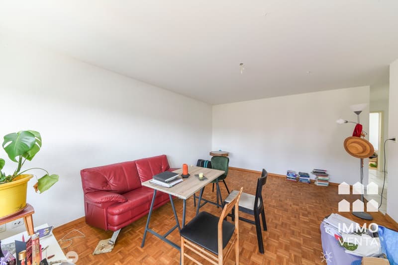 Red leather couch, wooden table, 2 chairs, books, plant, floor lamp, white walls, wooden floor