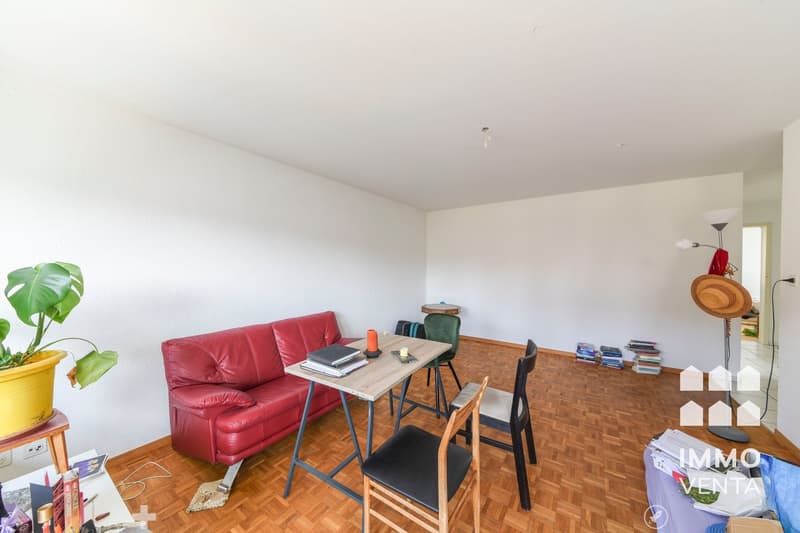 Red leather couch, wooden table, 2 chairs, books, plant, floor lamp, white walls, wooden floor