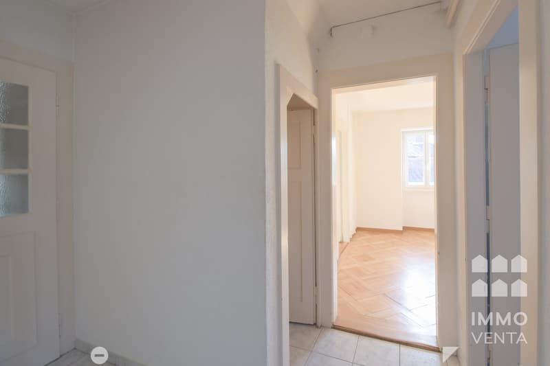 Empty room with white walls, wooden floor, and two doors leading to other rooms.