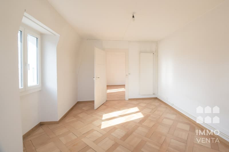 Empty room with wooden parquet flooring, white walls, two windows, and an open door leading to another room.