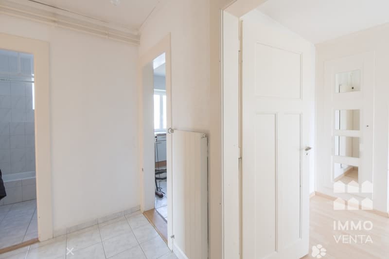 Empty room with white walls, white tiles, white doors, and wooden floor.