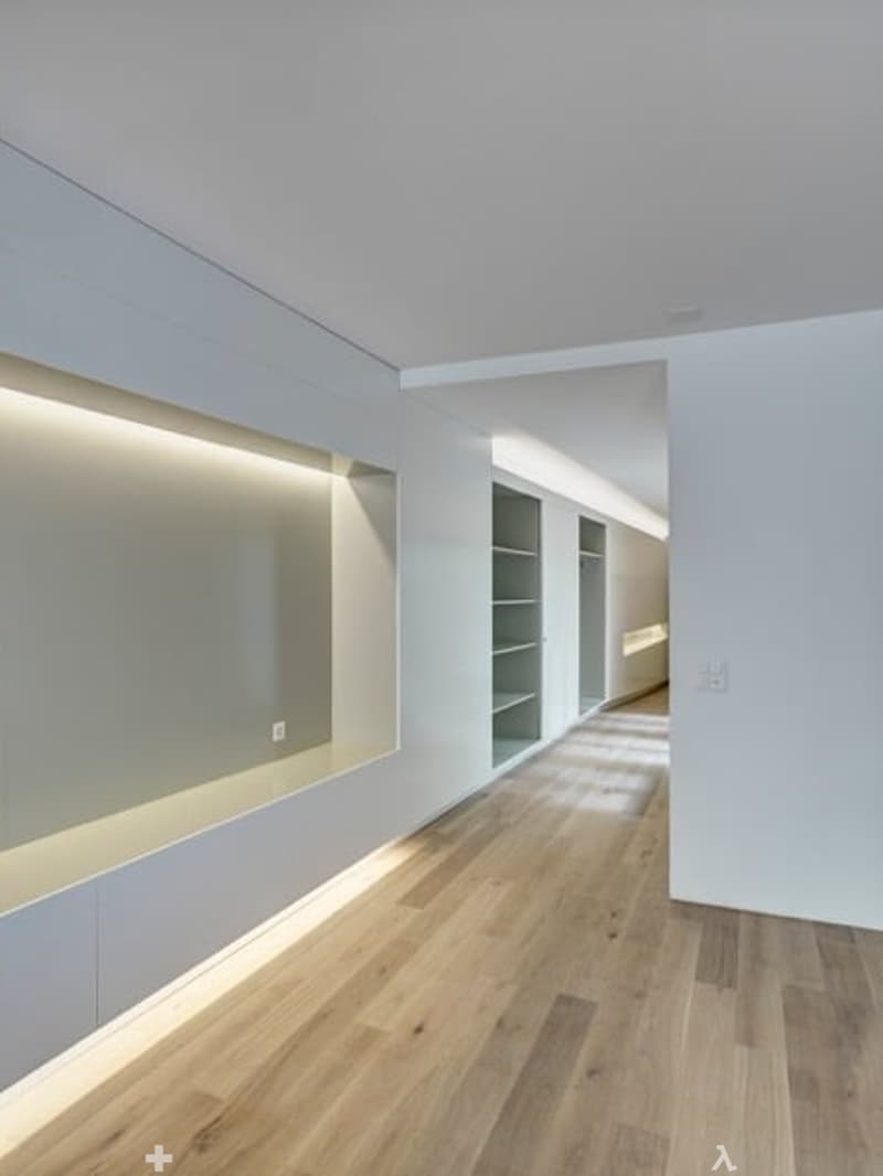 Empty room with wooden floor, white walls, built-in shelves, and recessed lighting