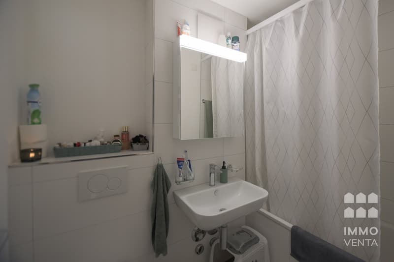 white tiles, white sink, mirror with light, shower curtain, towel, toiletries