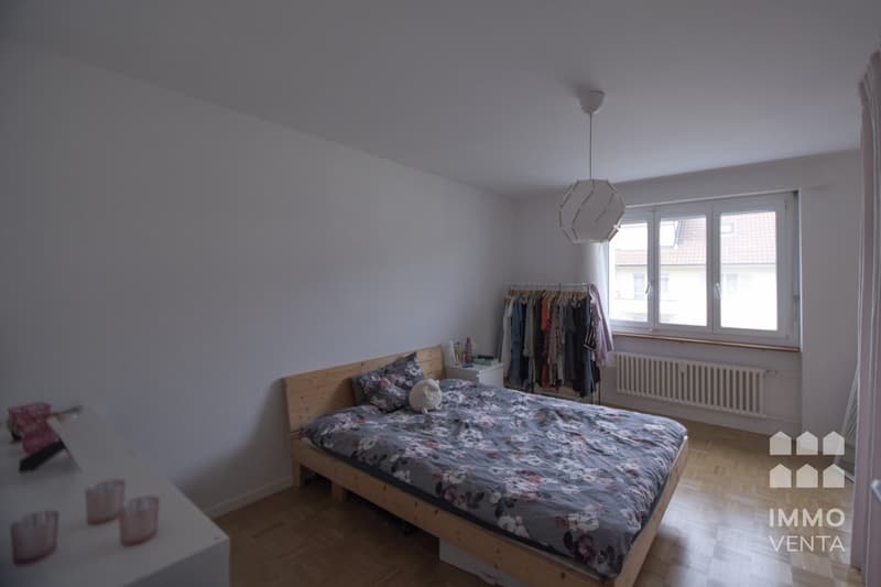 bedroom with bed, nightstand, radiator, window, clothes rack, lamp