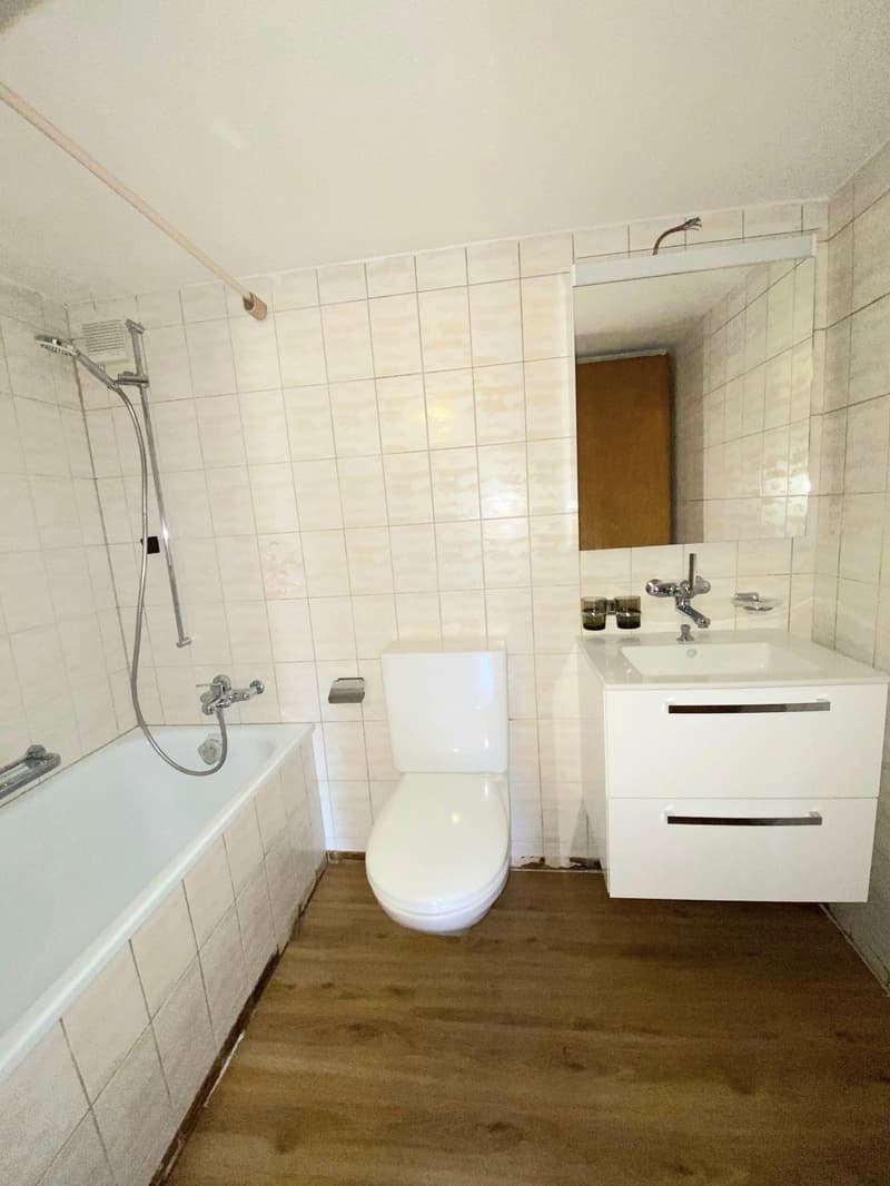 Tiled bathroom with white walls, a bathtub, a toilet, a vanity with drawers, and a sink with a faucet.