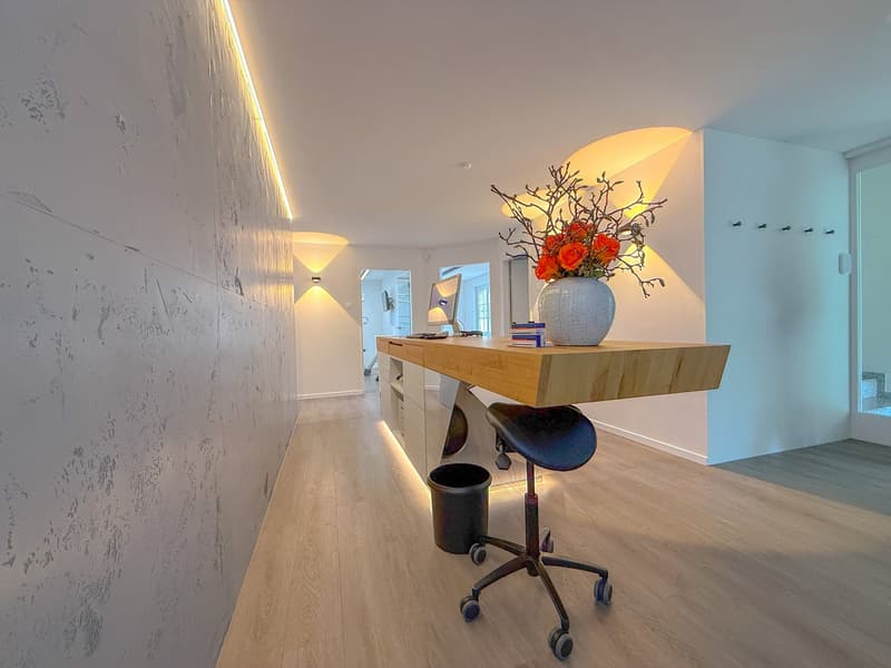 large room, long desk, white wall, desk with vase, trash can, chair, monitor