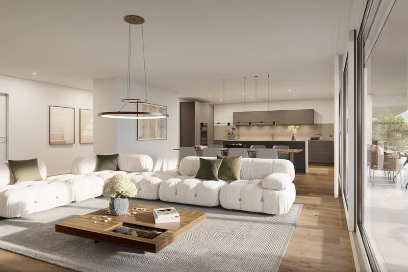 Spacious open-concept living room with large sectional sofa, wooden coffee table, and modern pendant lighting. The kitchen is visible in the background with sleek gray cabinets and appliances. Large windows provide natural light and access to a balcony or