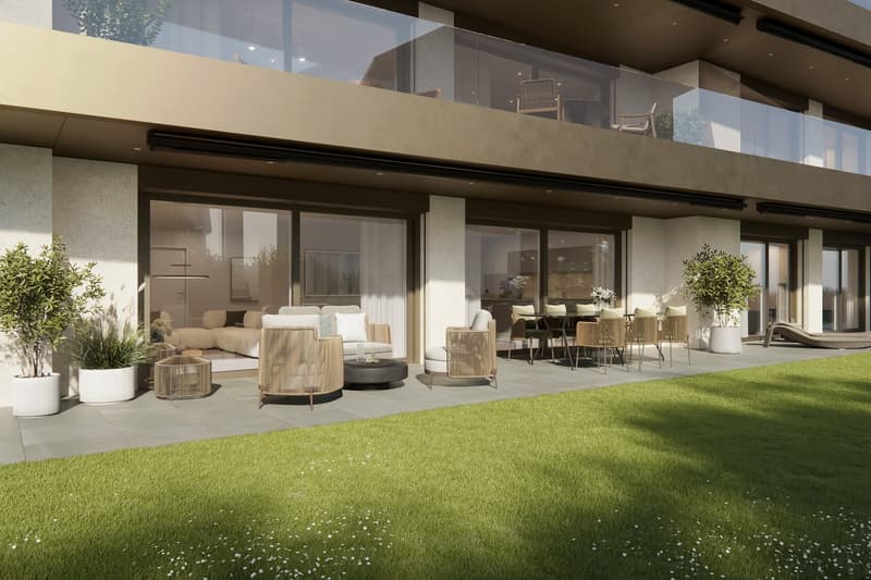 Modern two-story house with large glass windows, balcony, and outdoor seating area. The house has a spacious lawn with a well-manicured grass area. The interior is visible through the glass windows, showing a living room and dining area furnished with con