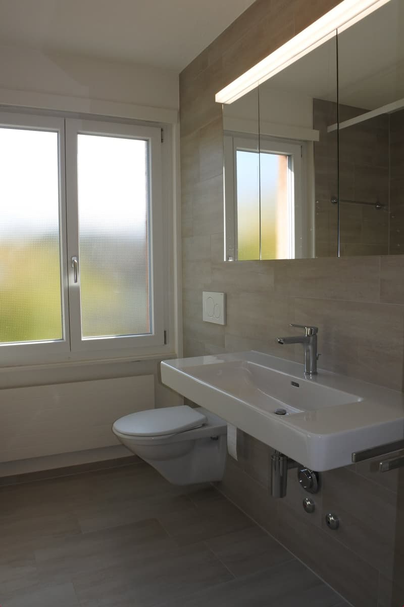 modern bathroom with white sink, silver faucet, white toilet, large mirror, white radiator, tiled floor