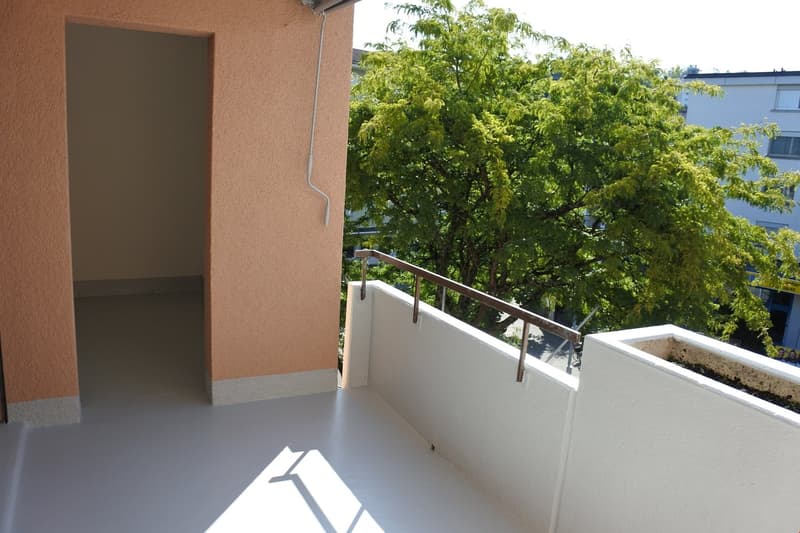 Balcony with railings, white floor, view of a tree and a building