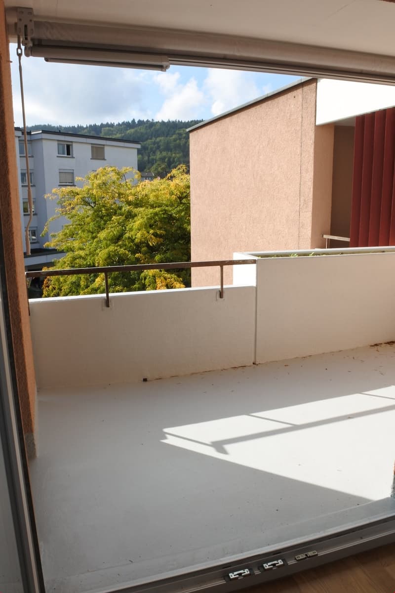 Balcony with white floor, metal railing, view of a tree and a building