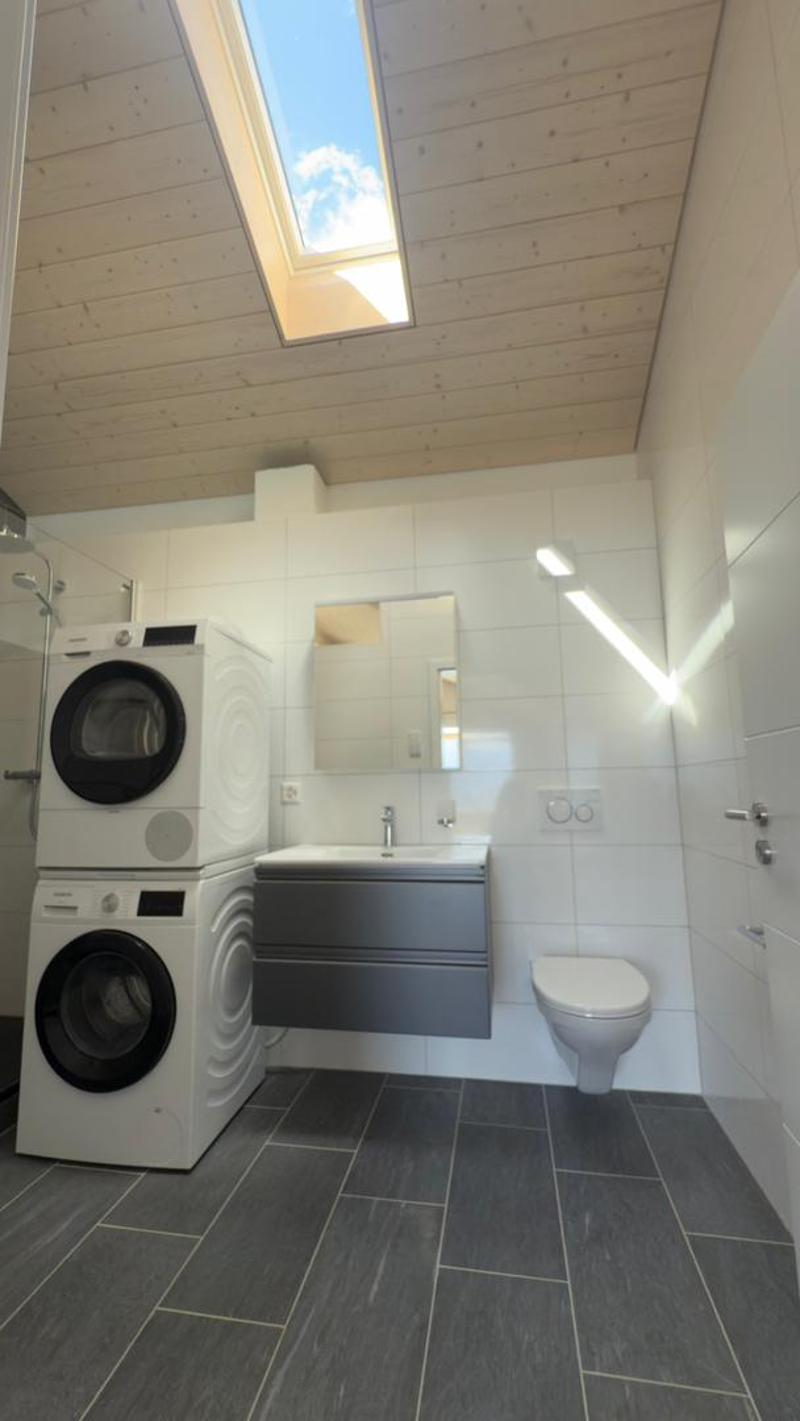 Bathroom with white tiles, a washing machine, a sink, a toilet, and a skylight