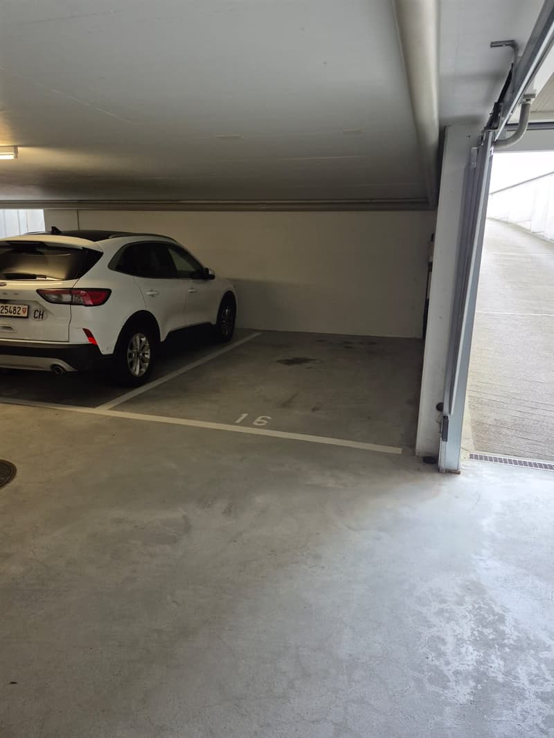 The image shows a garage space with a white SUV parked in a numbered parking spot. The garage has a concrete floor and a white ceiling.