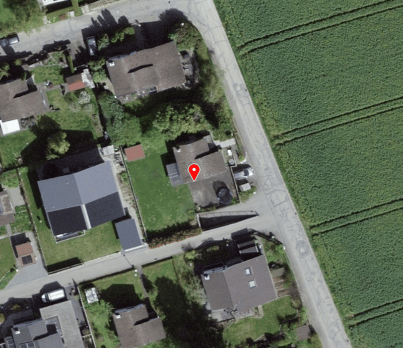 Row of detached houses, one marked with a red location pin, some have garages, one has a carport.