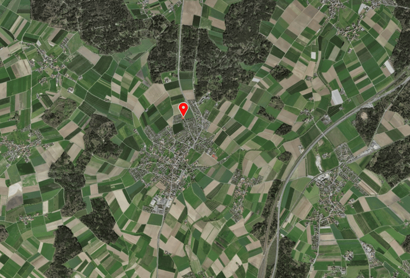 Aerial view of a green countryside with farmlands and roads. Location marked with a red pin.