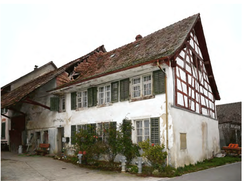 Old house, damaged roof, white walls, red brick accents, multiple windows, overgrown plants