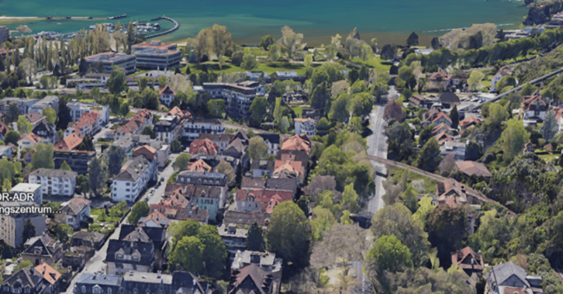 Aerial view of a town with many buildings, trees, and a road, with a lake in the background.