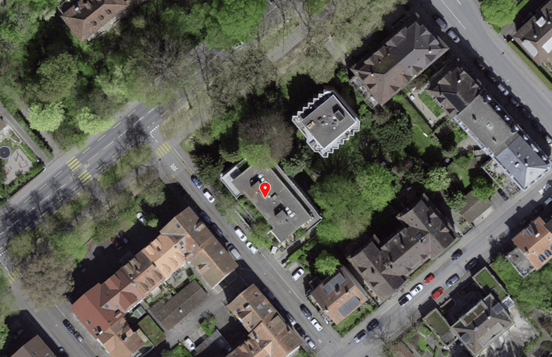 House located in a residential area, surrounded by trees and other houses, with a driveway and parking spaces.